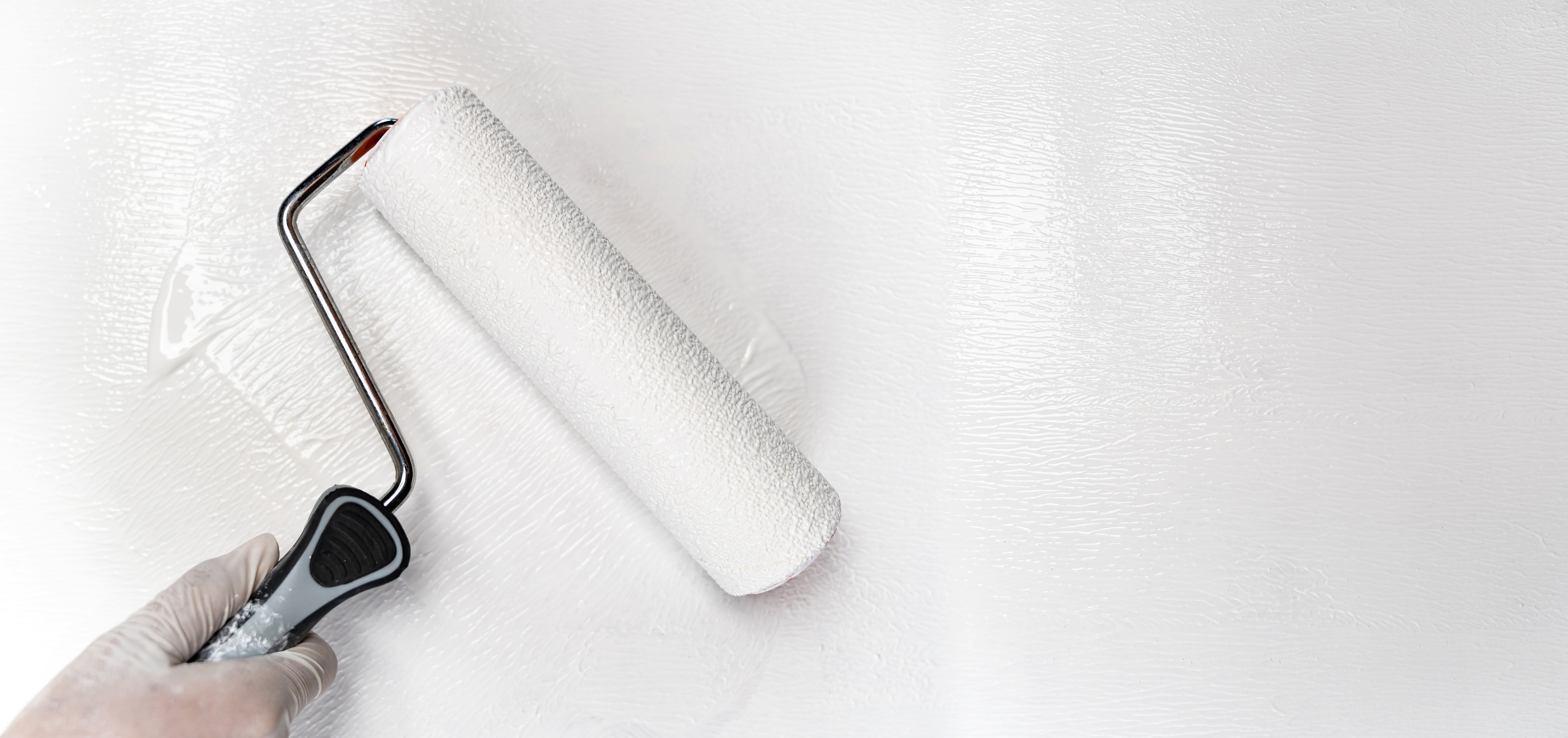 Hand wearing a white glove painting a white wall with a paint roller.