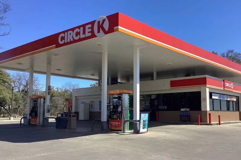 Circle K gas station with fuel pumps under a red branded canopy and the store behind it on a sunny day.