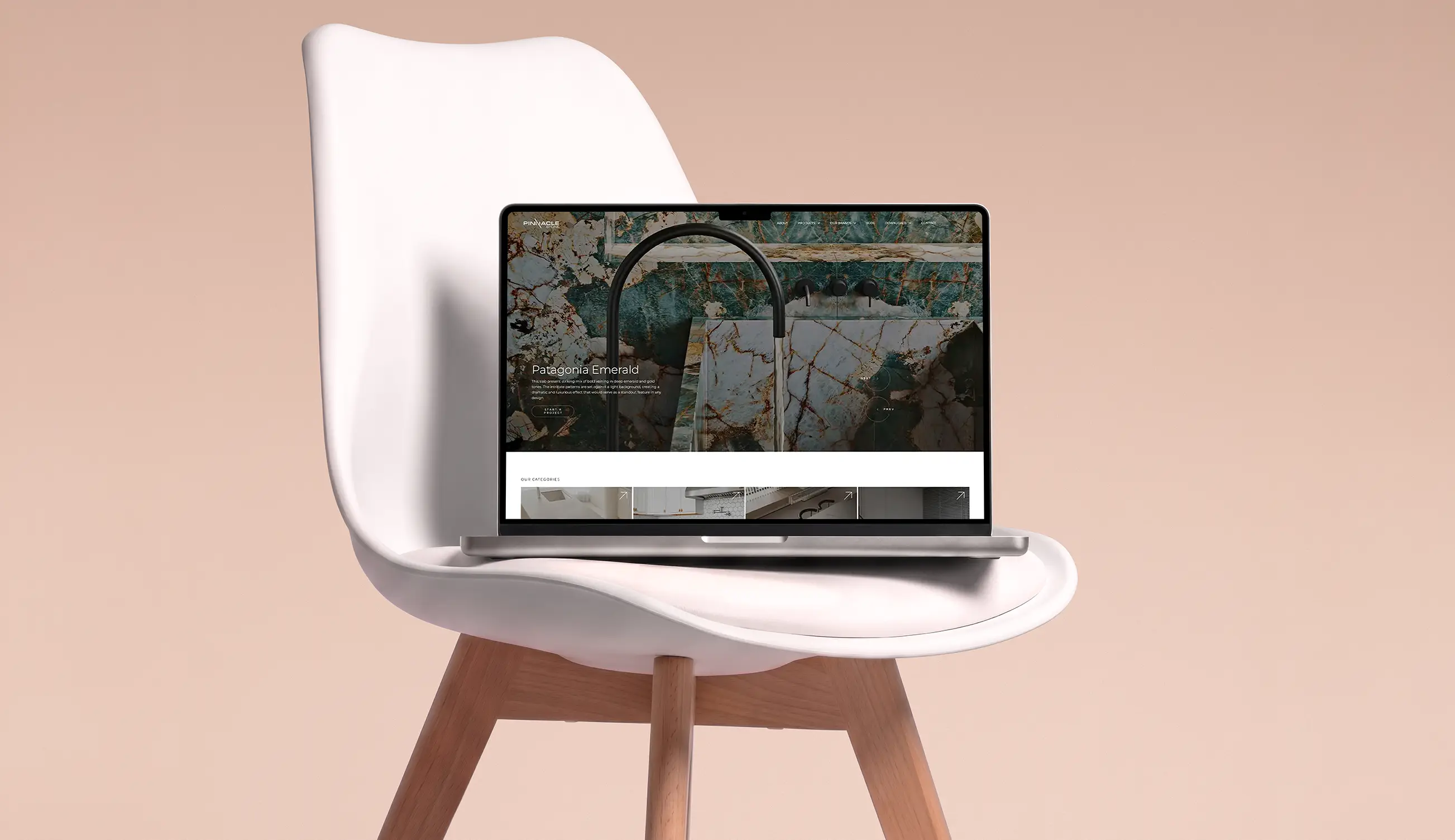 Modern silver laptop displaying a webpage with a marble sink image and text titled 'Patagonia Emerald' placed on a white chair with wooden legs against a light peach background.