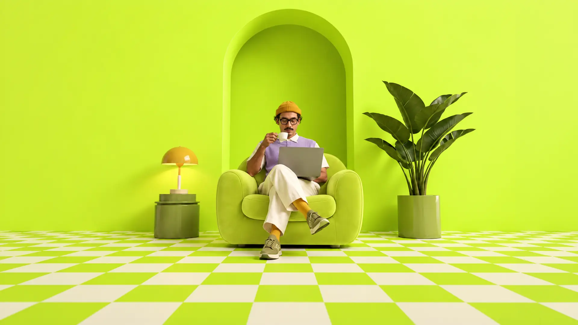 Man sitting on a green armchair in a bright lime green room with checkered floor, drinking coffee and using a laptop, next to a yellow lamp on a green side table and a large potted plant.