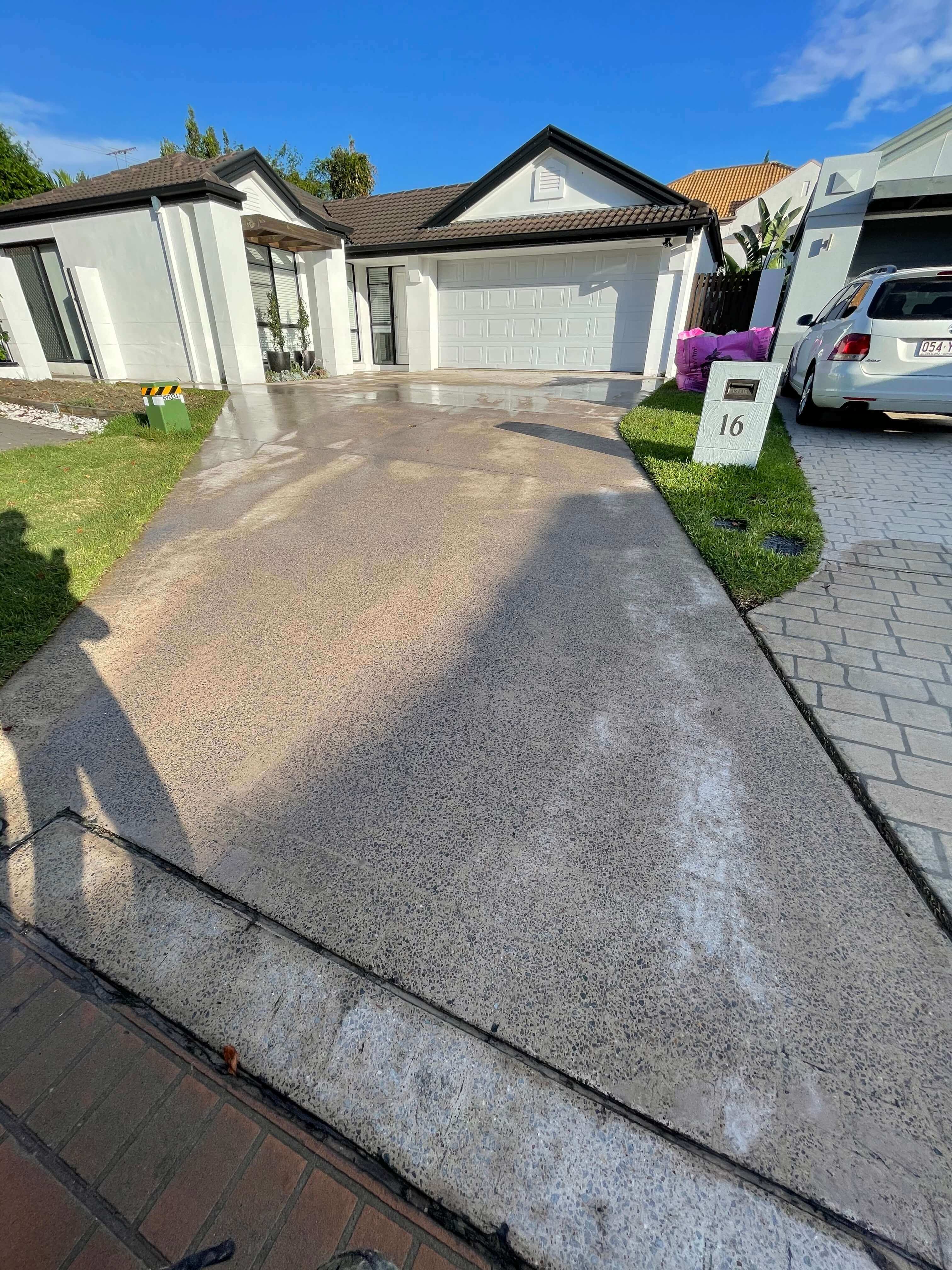 Concrete driveway with a light coating in front of a white garage and house under clear blue sky.
