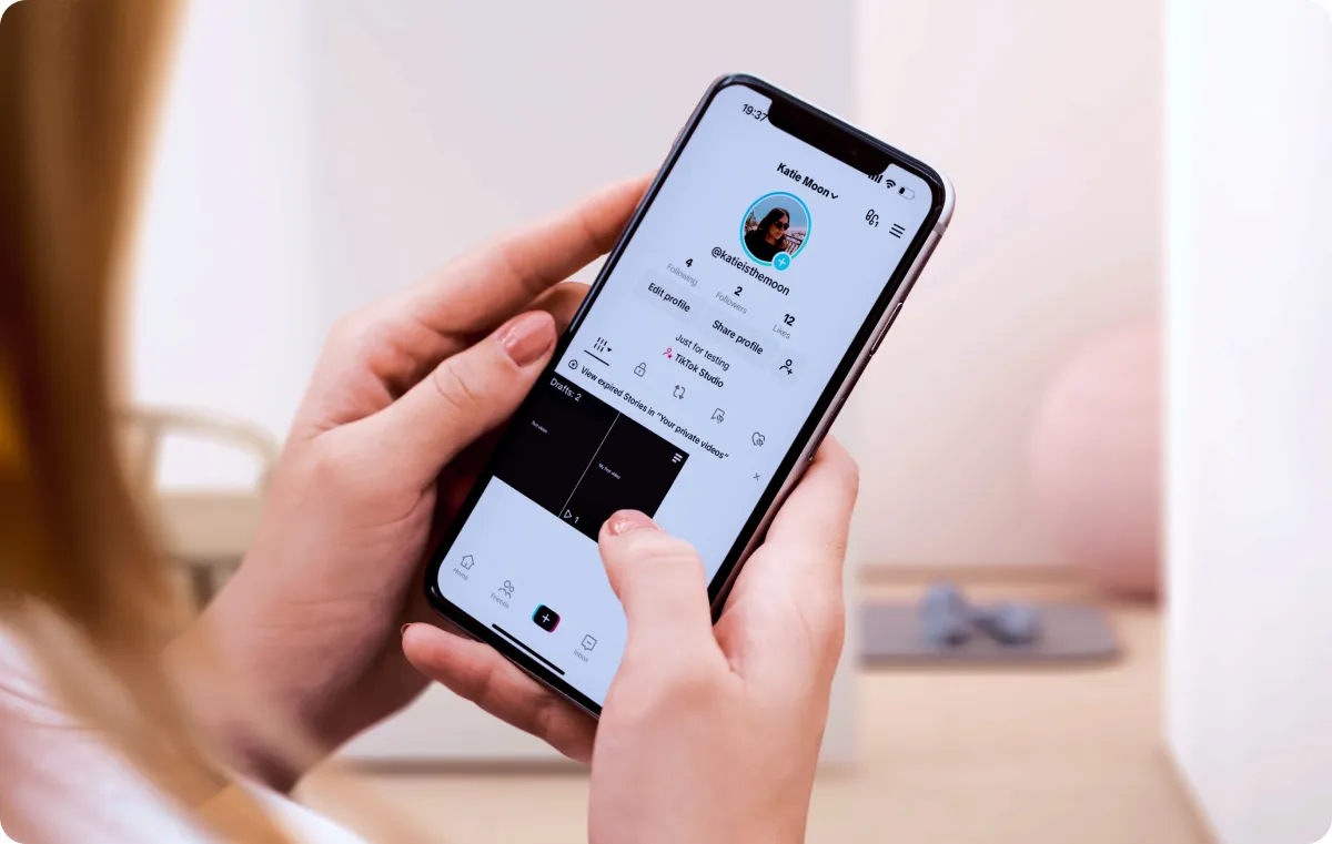 Close-up of a hand holding a phone displaying a TikTok profile, with video drafts visible.