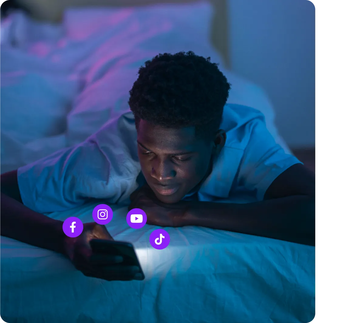 Young man lying in bed at night, looking at his phone with social media icons floating nearby.
