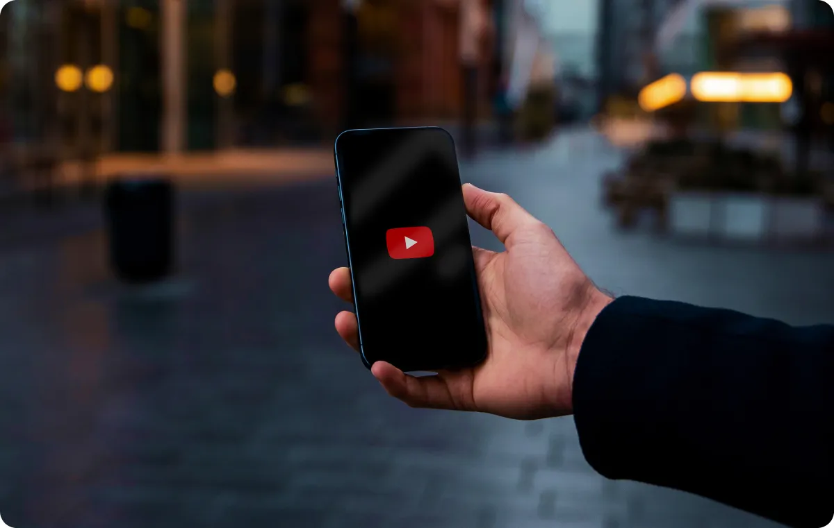 An image of hands holding a phone with a YouTube logo on the screen.