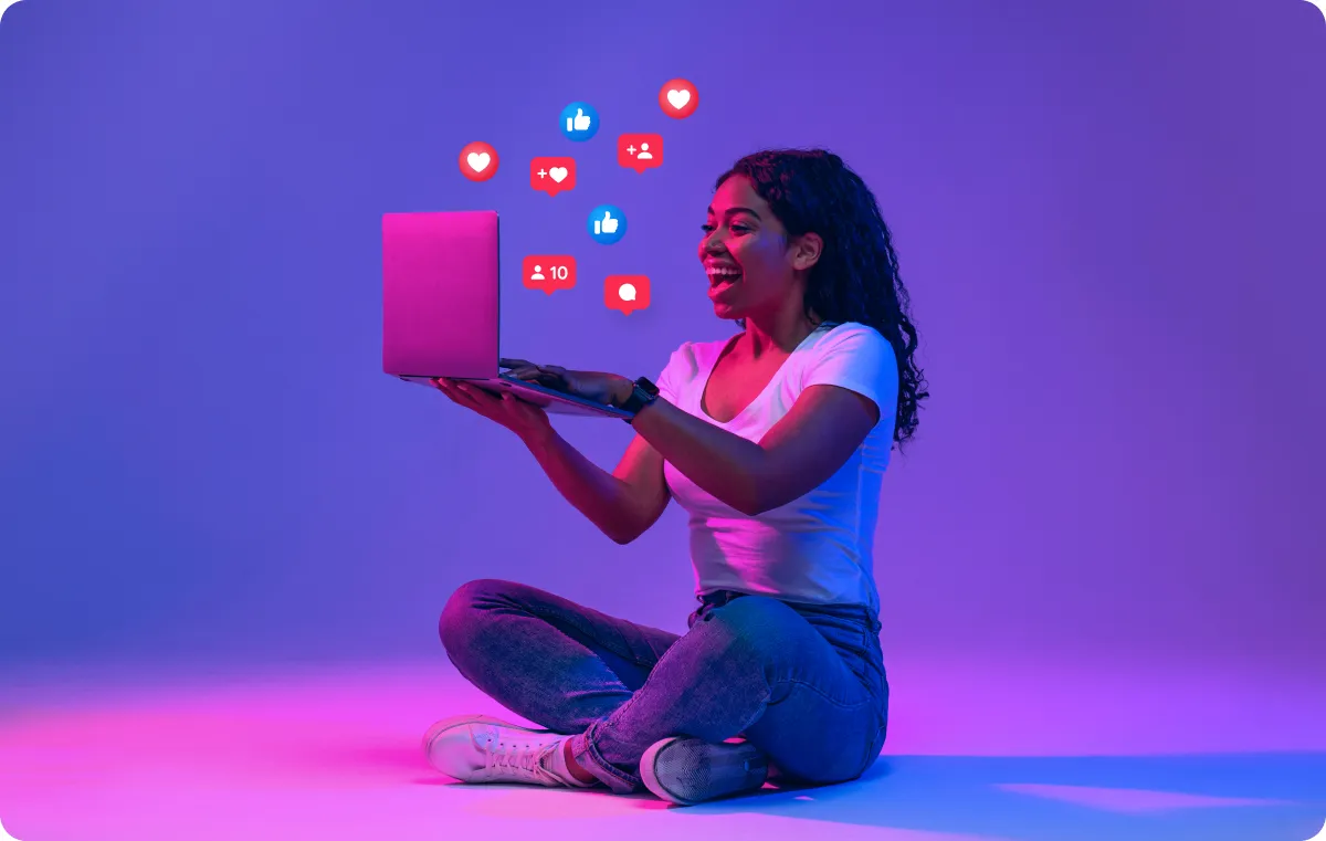 A person using a laptop with social media emojis popping up, symbolizing social media approval and engagement.