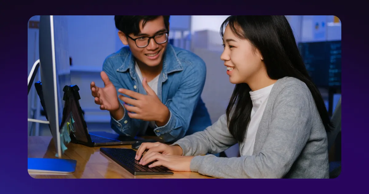 A person pointing to a computer while chatting with another person.