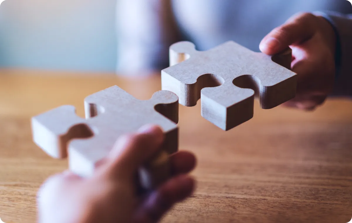 Puzzle pieces fitting together, with two men holding them, symbolizing business alignment.