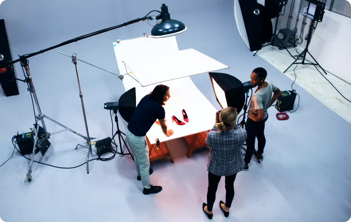 A product photoshoot setup with a white background, professional lighting equipment, and three people working around the product.