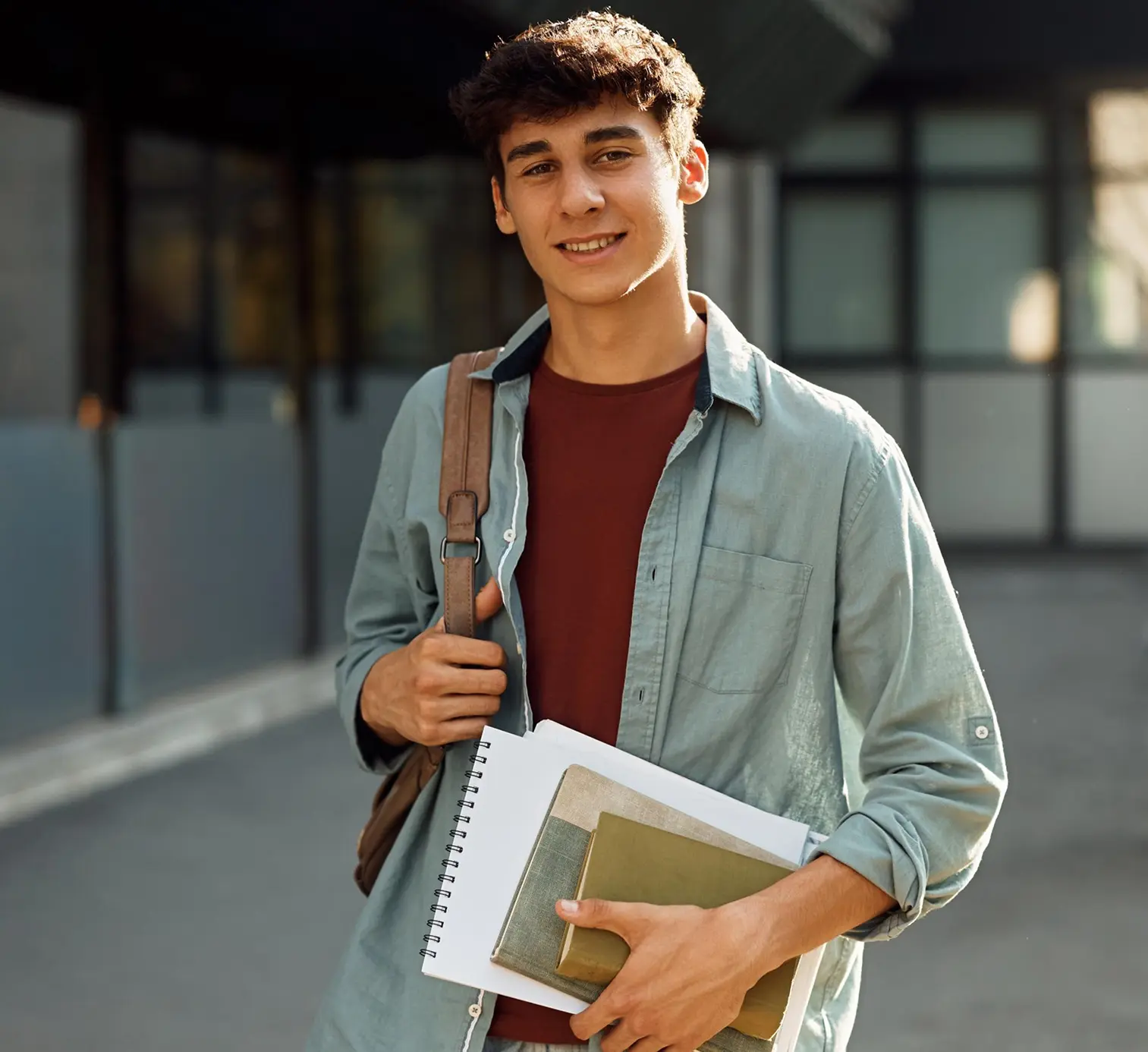A secondary student holding books and a notebook outside a campus building.