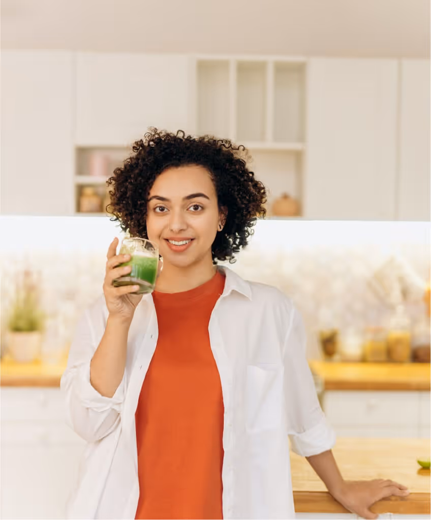 A woman standing in the kitchen, holding a green juice and smiling
