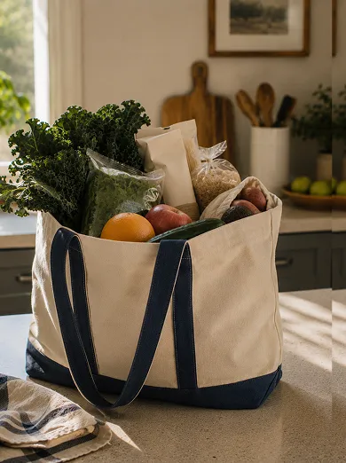 Canvas tote bag with dark blue handles filled with fresh groceries including kale, oranges, cucumbers, onions, grains, and sweet potatoes on a kitchen countertop.