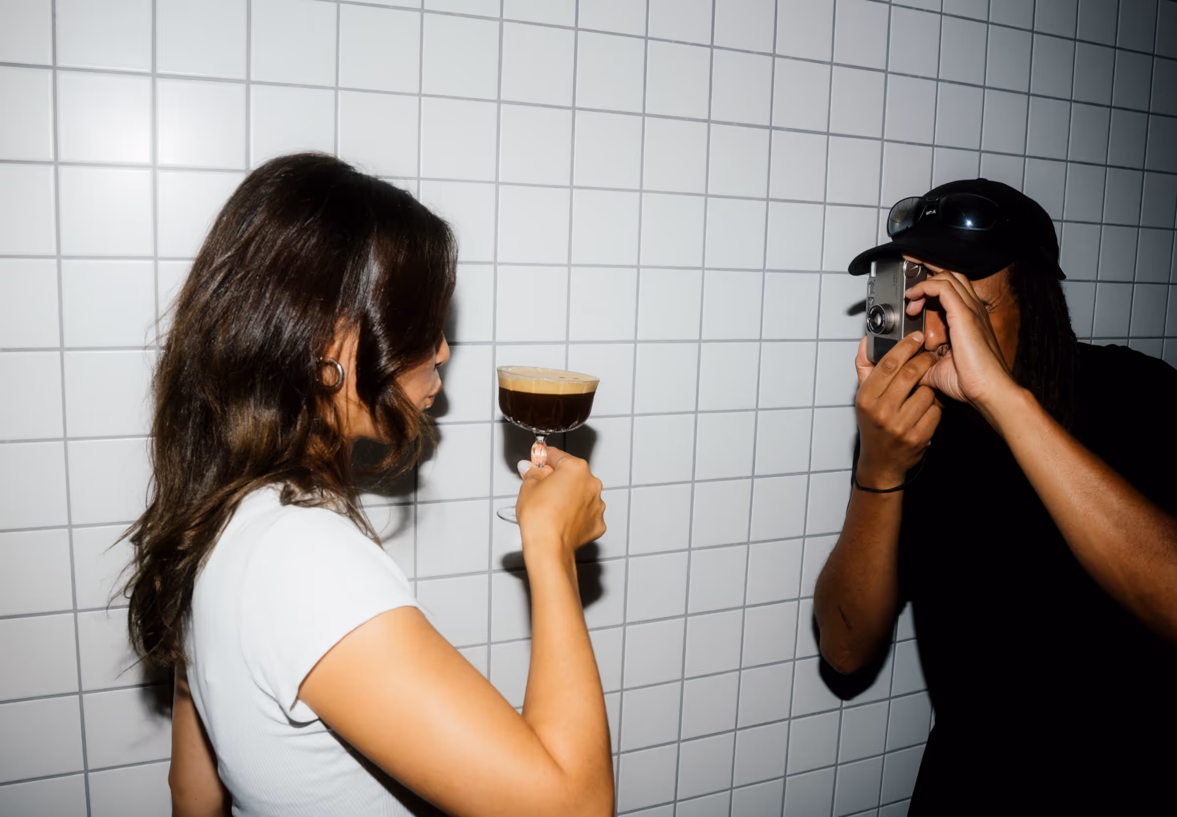a man taking a picture of a woman with a glass of liquid