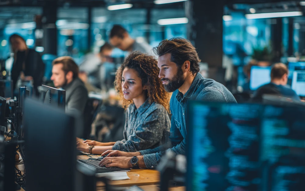 Team of data analysts collaborating on automated data extraction processes in a modern office, using advanced software and real-time data on multiple computer screens.
