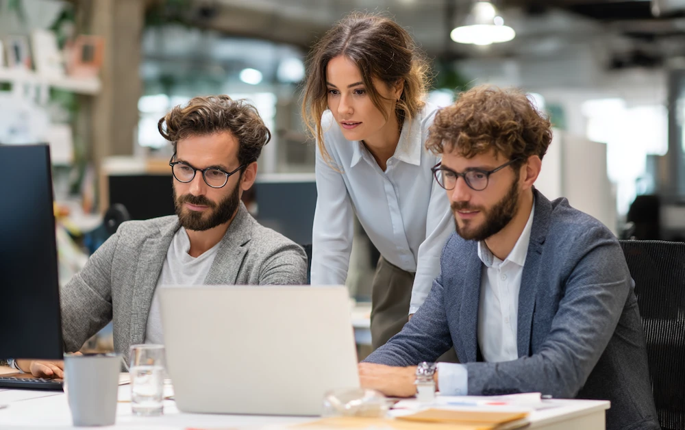 Team of finance professionals collaborating on a monthly close checklist template, reviewing financial reports and reconciling data on laptops in a modern office.