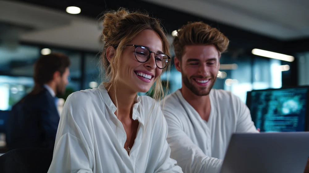 Smiling finance professionals using accounting software for automation and accounting processes on a laptop in a modern office environment.