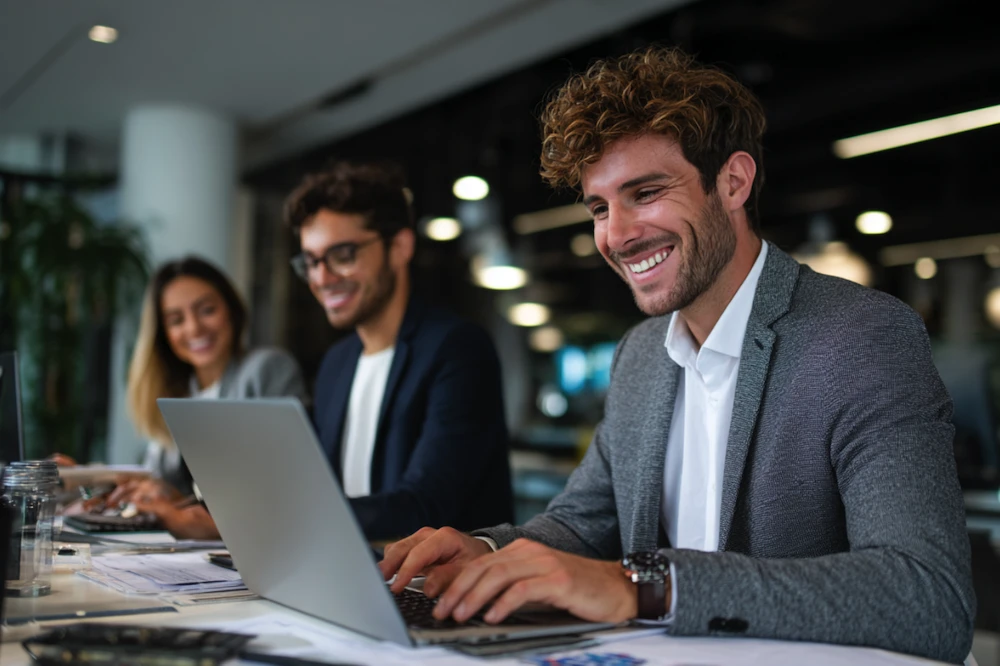 Happy professionals working on laptops in a modern office, symbolizing collaboration and financial planning—ideal visual for understanding what a rebate is and how it benefits businesses.