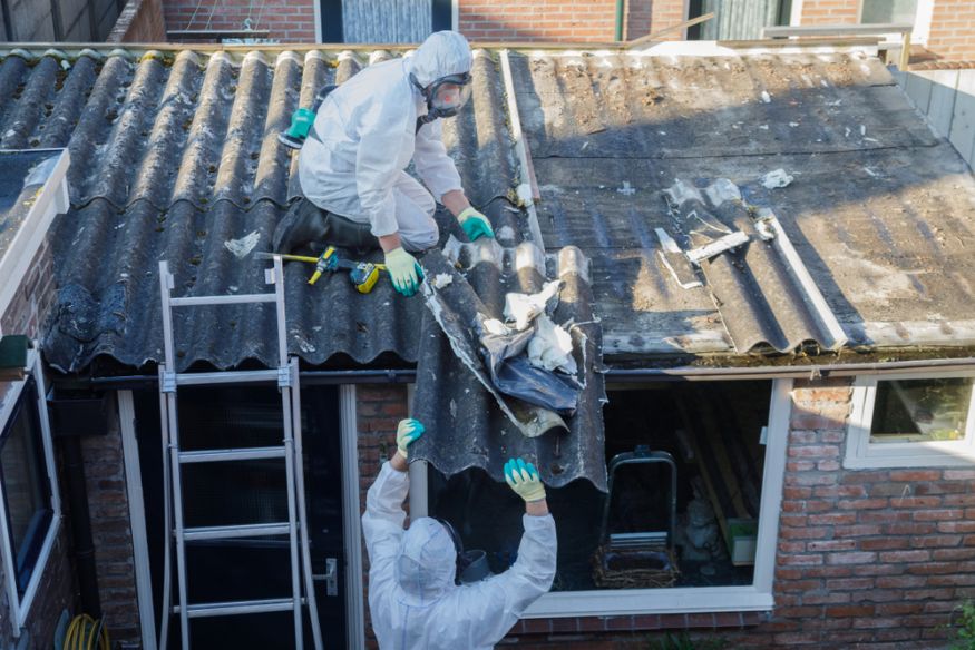 Two asbestos removal workers in protective suits taking down a corrugated asbestos roof