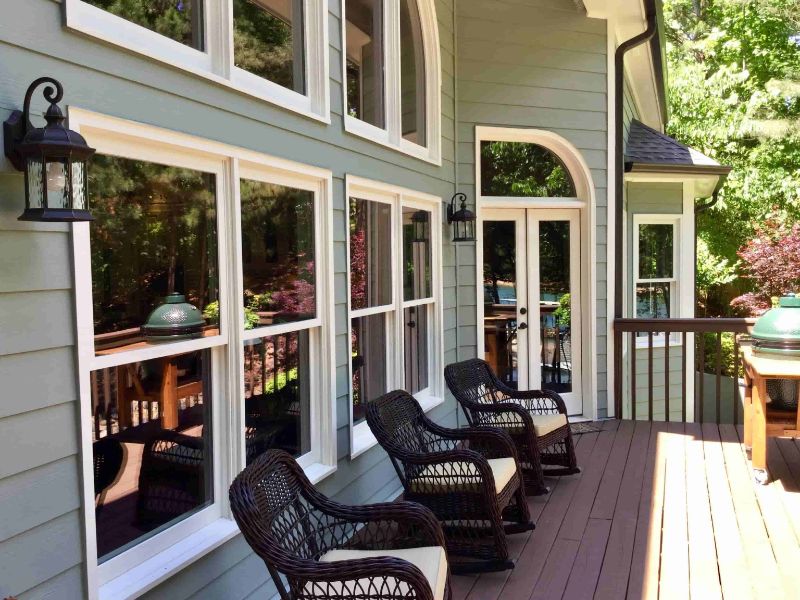 A home with new sage green siding, white windows and a wooden deck