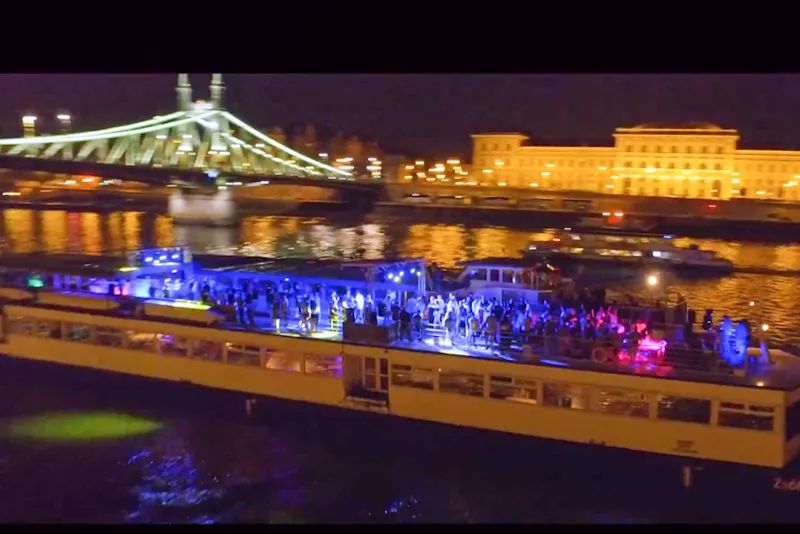 A boat is lit up with blue lights in front of a bridge