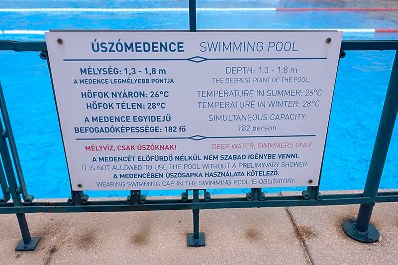 A sign is posted on a fence near a swimming pool