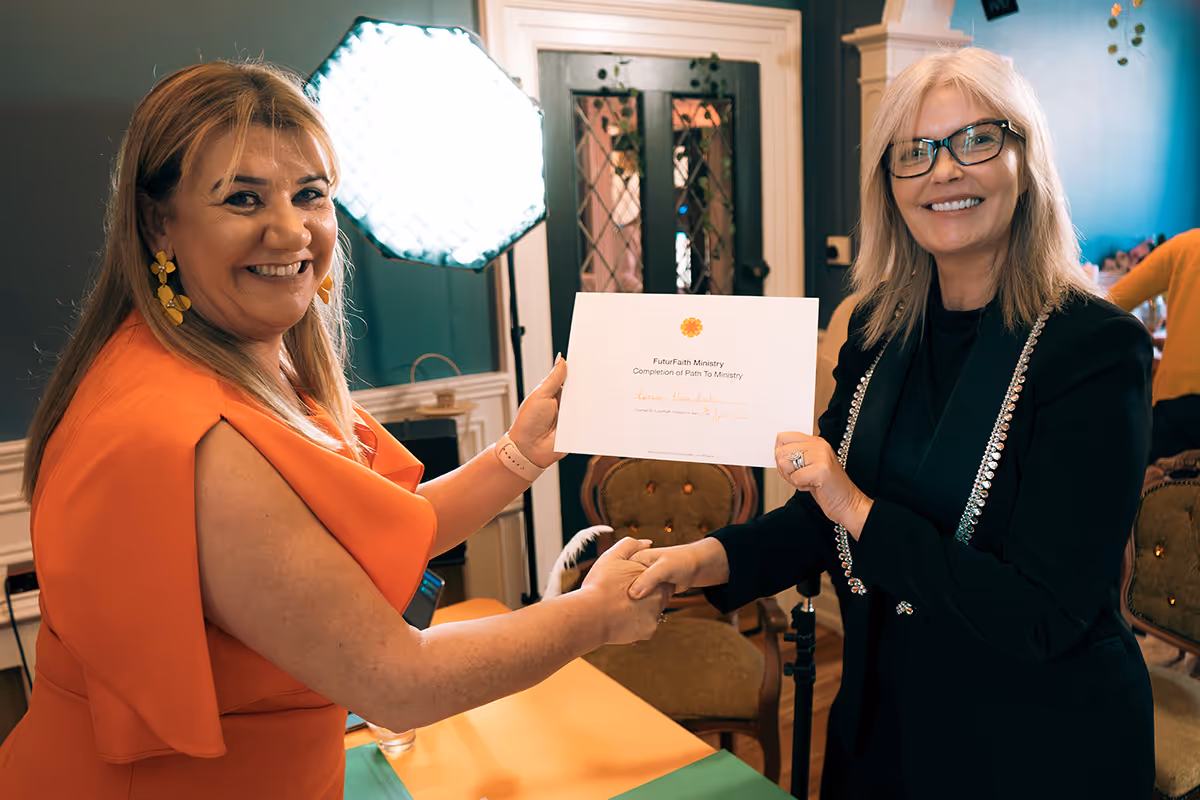 Two women smiling and shaking hands while holding a FutuFaith Ministry certificate of completion.