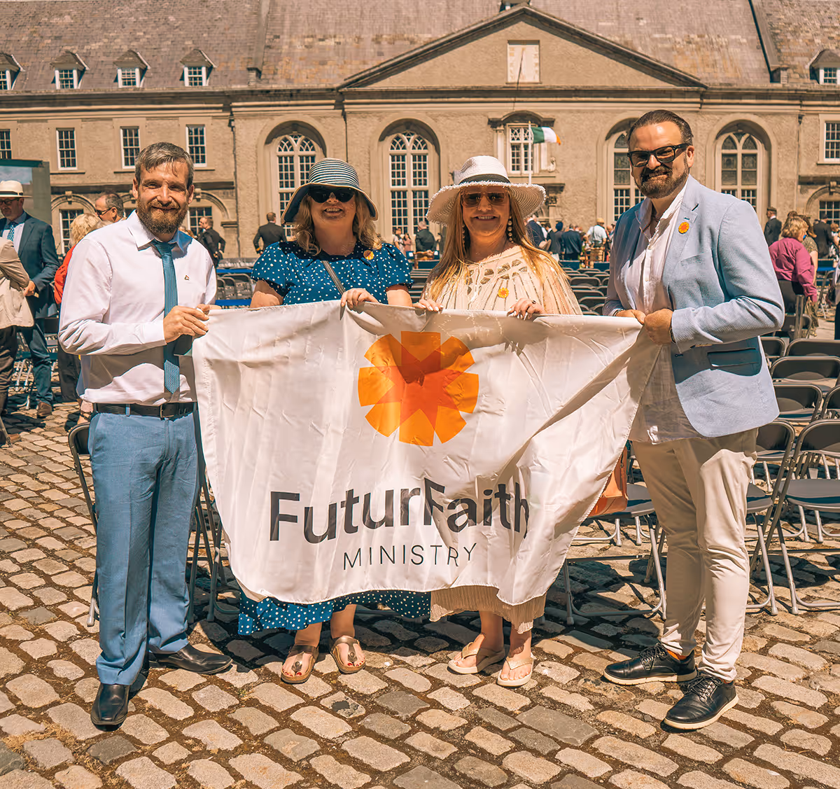 Four people standing on cobblestone holding a banner that reads 'FuturFaith Ministry' in front of a historic building.
