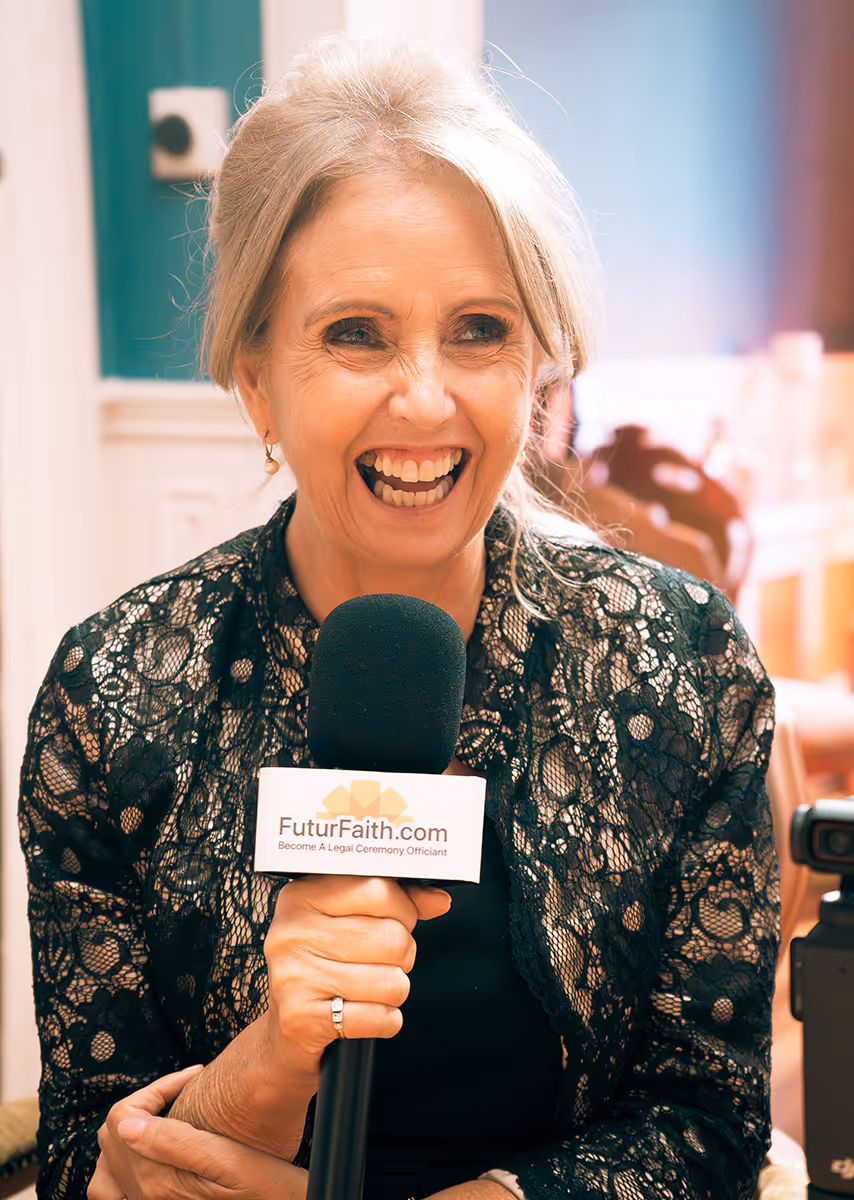 Smiling older woman with gray hair holding a microphone labeled FuturFaith.com indoors.