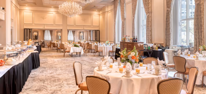 Elegant ballroom dining area with round tables set with white tablecloths, floral centerpieces, and neatly folded napkins.