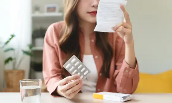 Woman sitting at a table reading the patient information leaflet from her medicine package