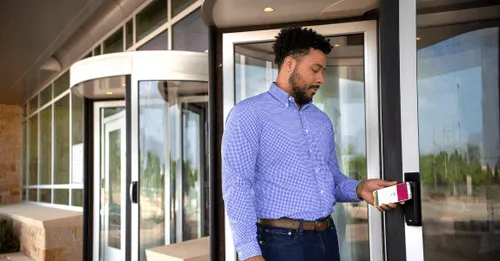 Man using his smartphone to tap and unlock a secure glass door at an office entrance.