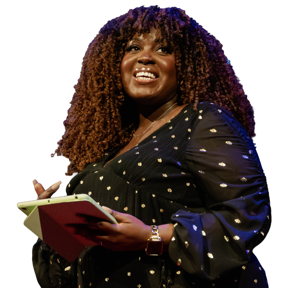 Keynote speaker Afua Hagan smiling on stage, holding a tablet and notebook.