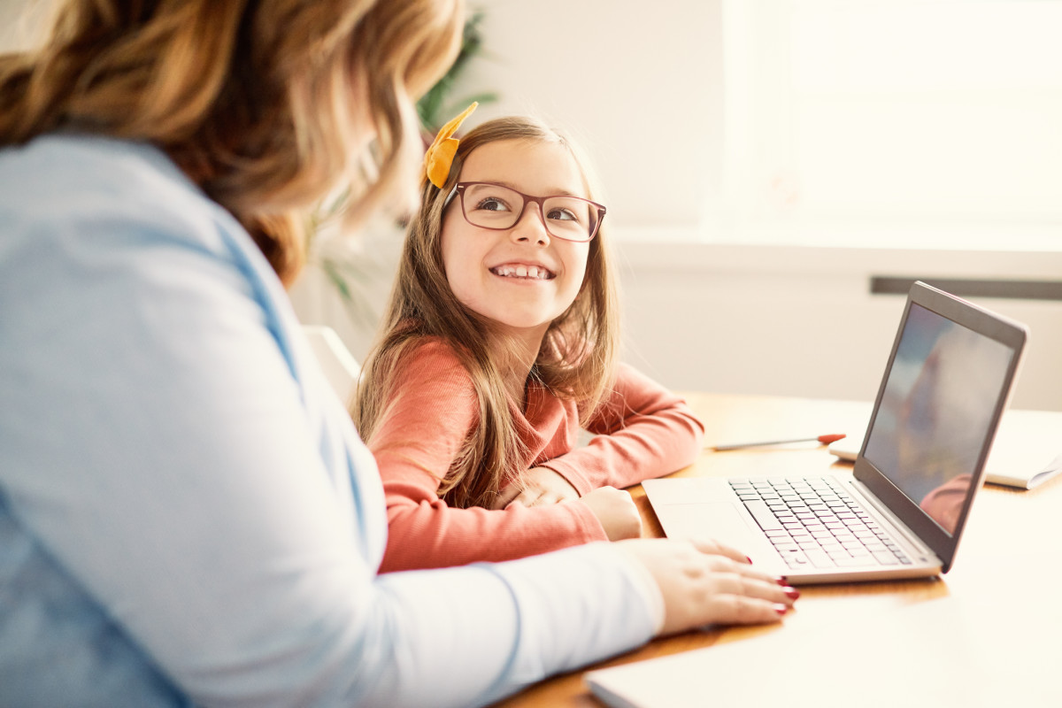 An image of a young student looking up a teacher who is pointing at a laptop screen