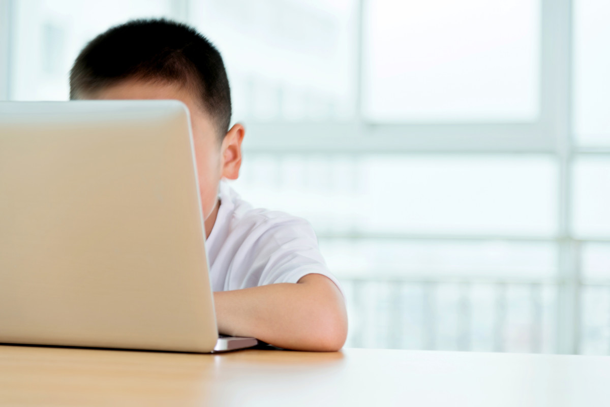 A yound student sits behind a laptop screen