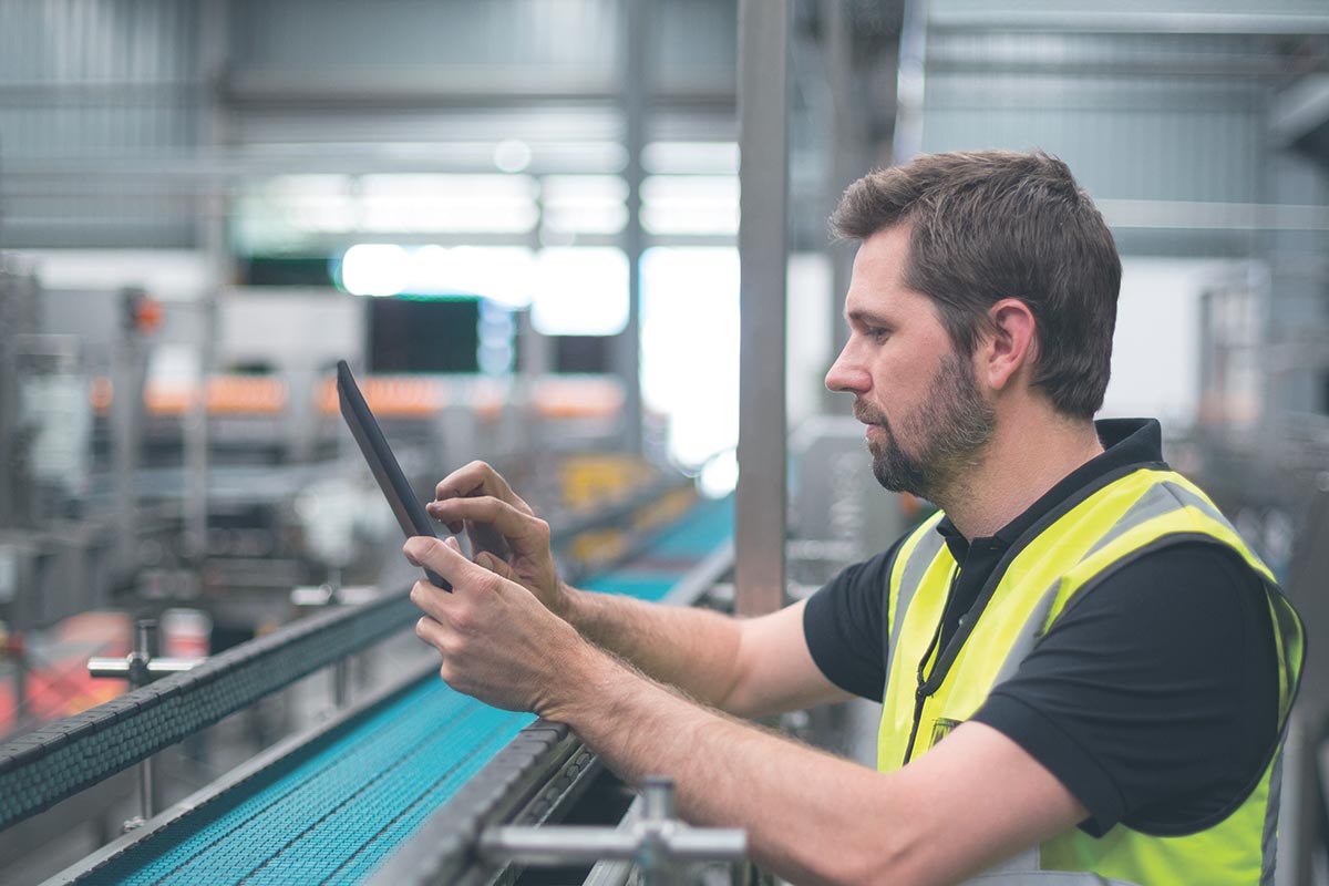 Person hält ein Tablet, das eine industrielle Überwachungssoftware mit Diagrammen und Asset-Informationen anzeigt.
