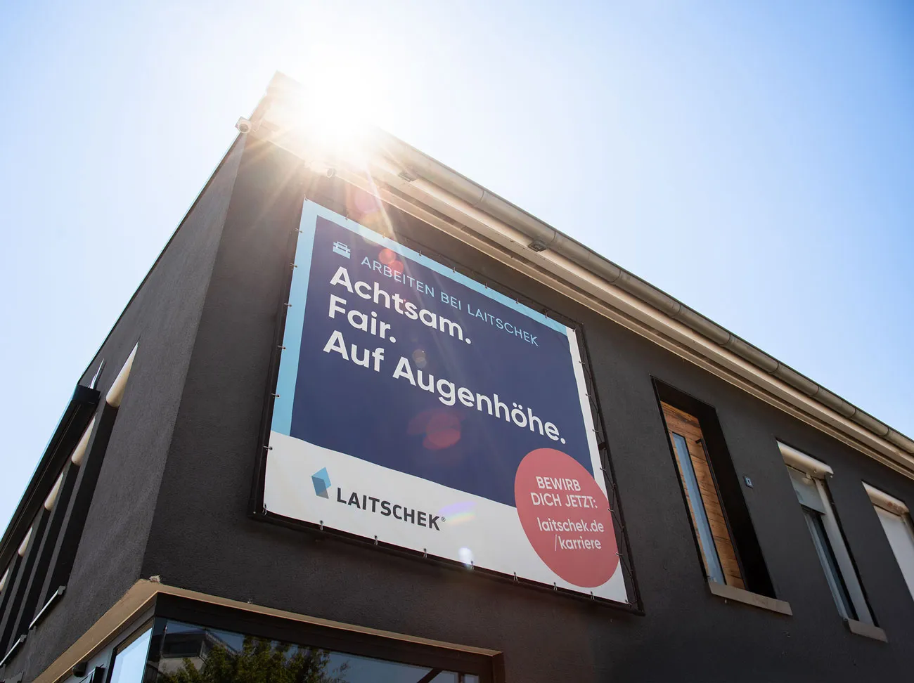 Ein schwarzes Gebäude mit einem Werbebanner von Laitschek mit der Aufschrift "Achstam. Fair. Auf Augenhöhe".