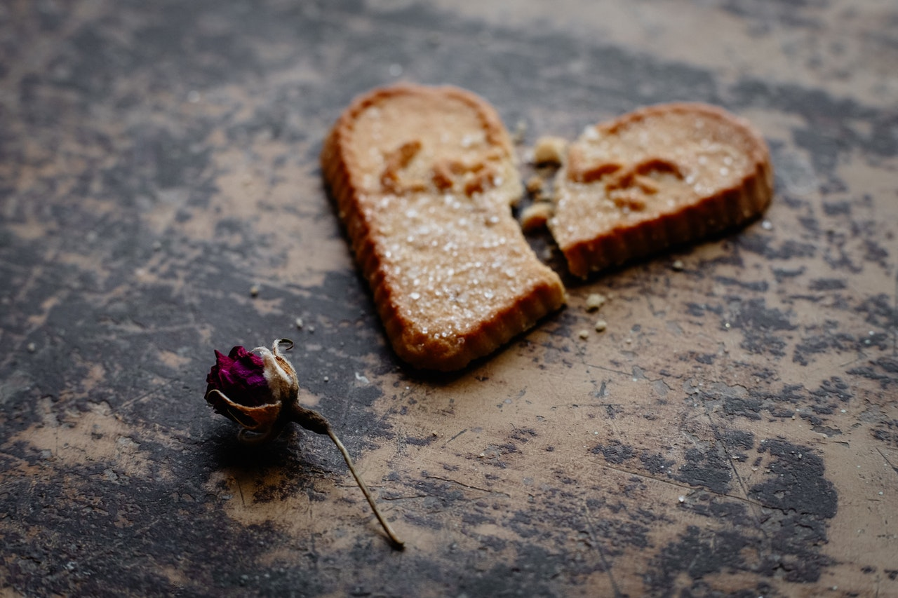 A cookie with "love" printed on it lies broken in half on a table. A dying rose lies on the below it. 