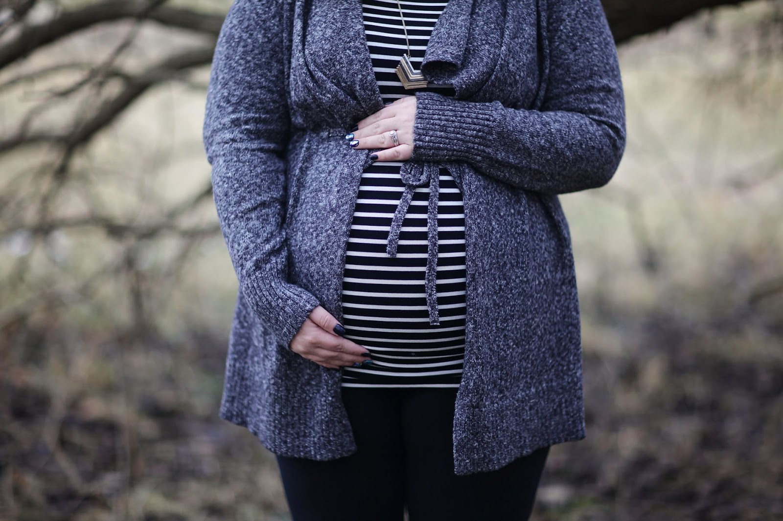 Depression during pregnancy is relatively common yet hardly talked about. Pregnant woman stands in wooded area with her hand on top of her stomach. 