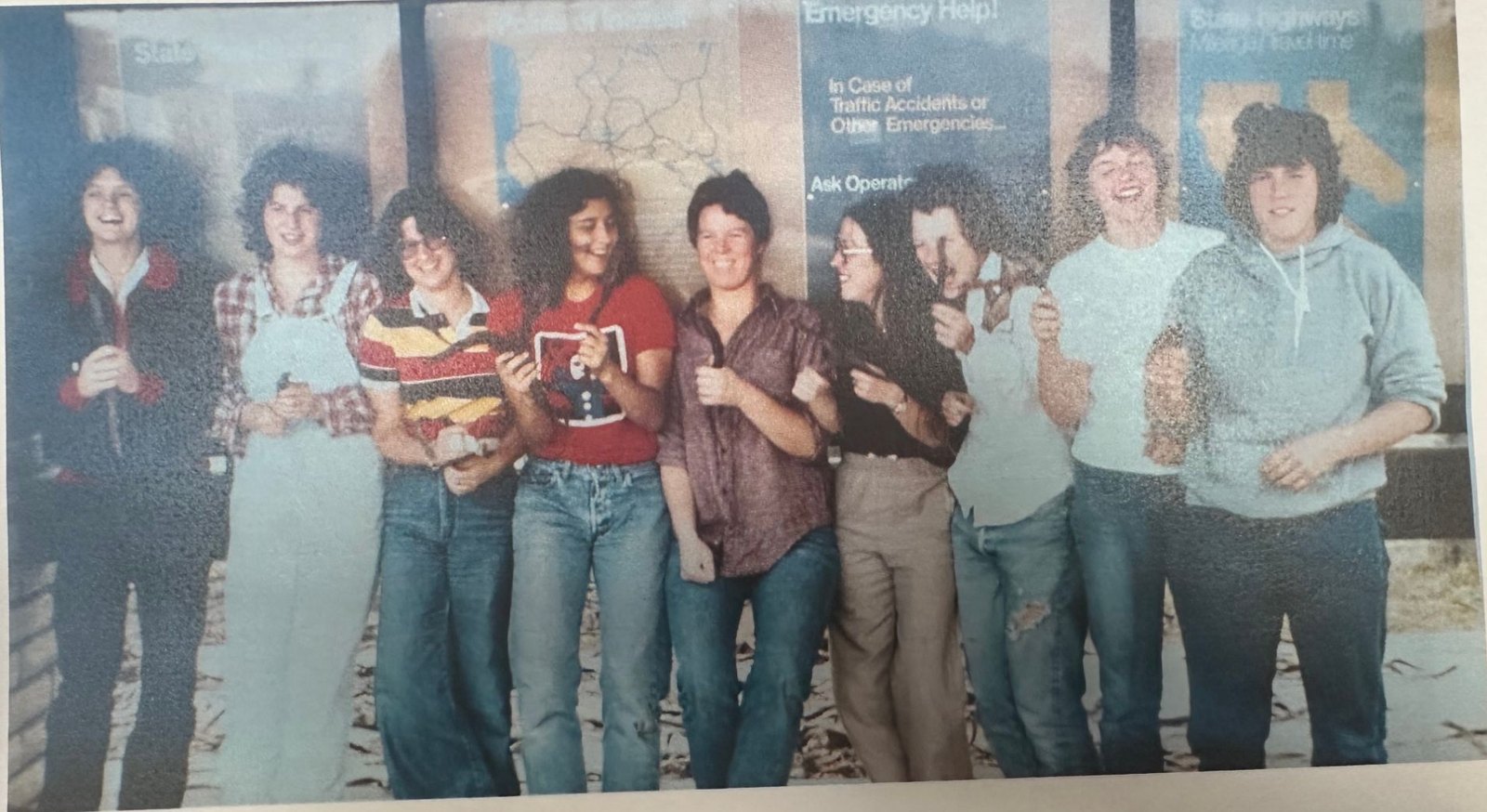 Nine Seattle Seabyrds players in 1970s street clothes, laughing and linking arms in front of highway information signs during a team road trip