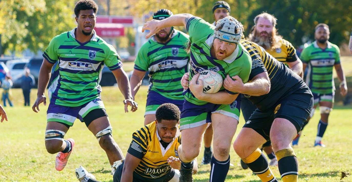A Seattle forward in a scrum cap carries the ball through a tackle at Tacoma, teammates in support, during Seattle's 82-0 win