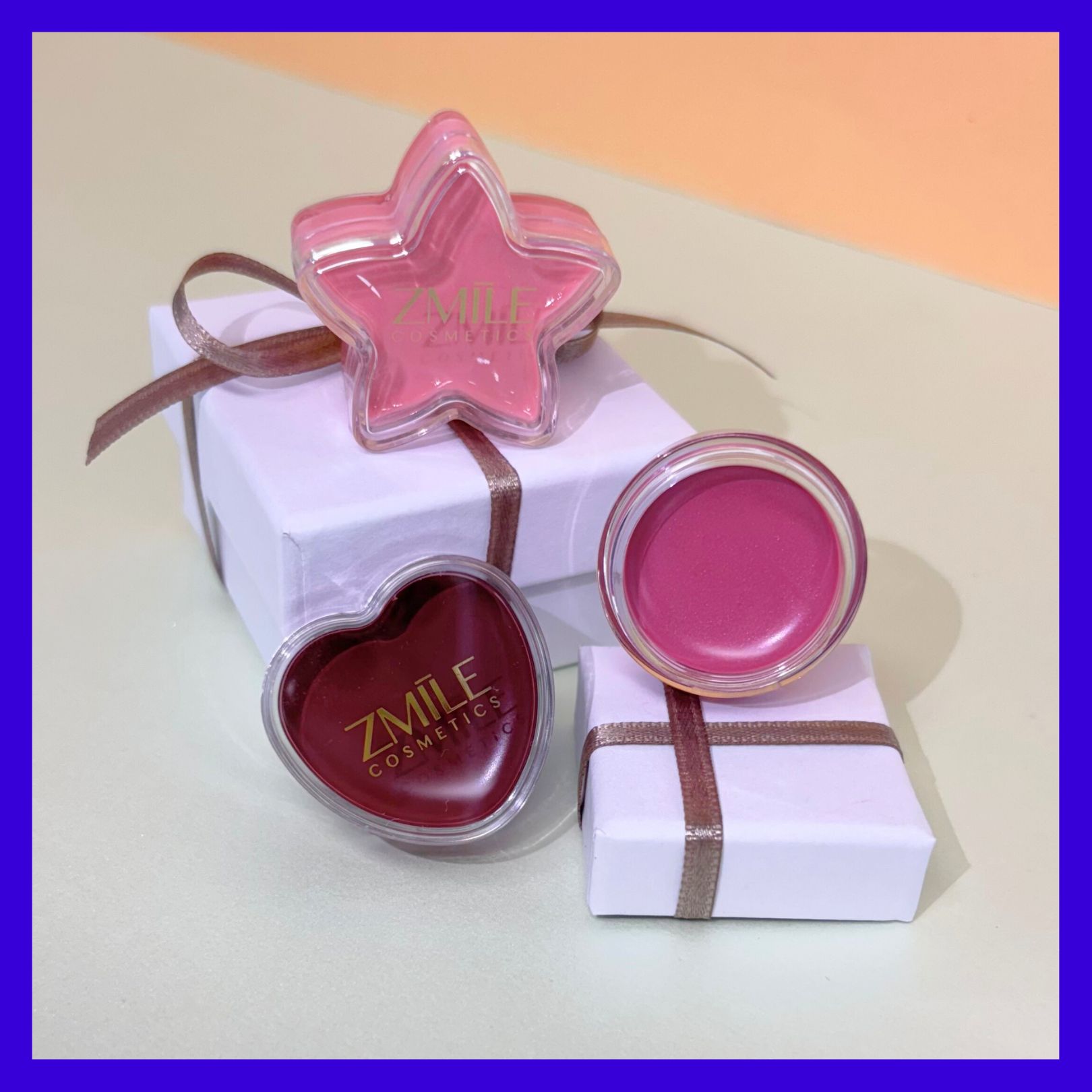 Drei Lipgloss Cremes in Rosa und Berry-Tönen in rundem, sternförmigen und herzförmigen ZMILE Cosmetics Case, präsentiert auf weissen Geschenkboxen.