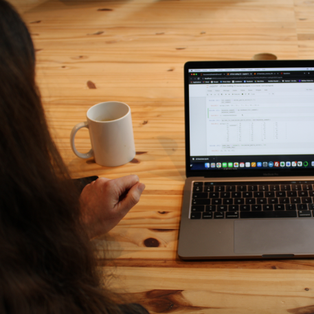 personne analysant un tableau de données sur un portable posé à côté d’une tasse blanche