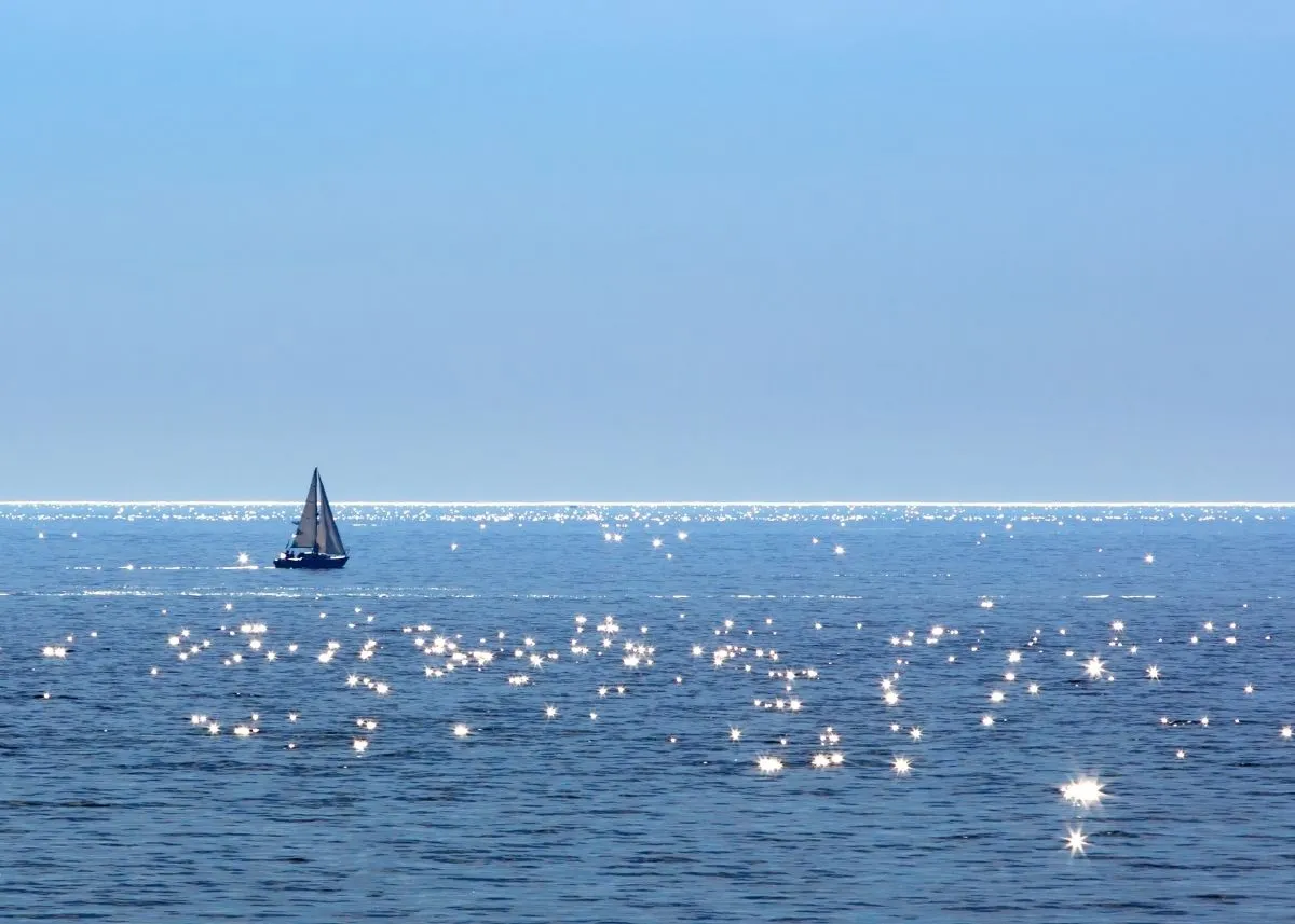 Sailboat gliding on sparkling blue ocean under clear sky.