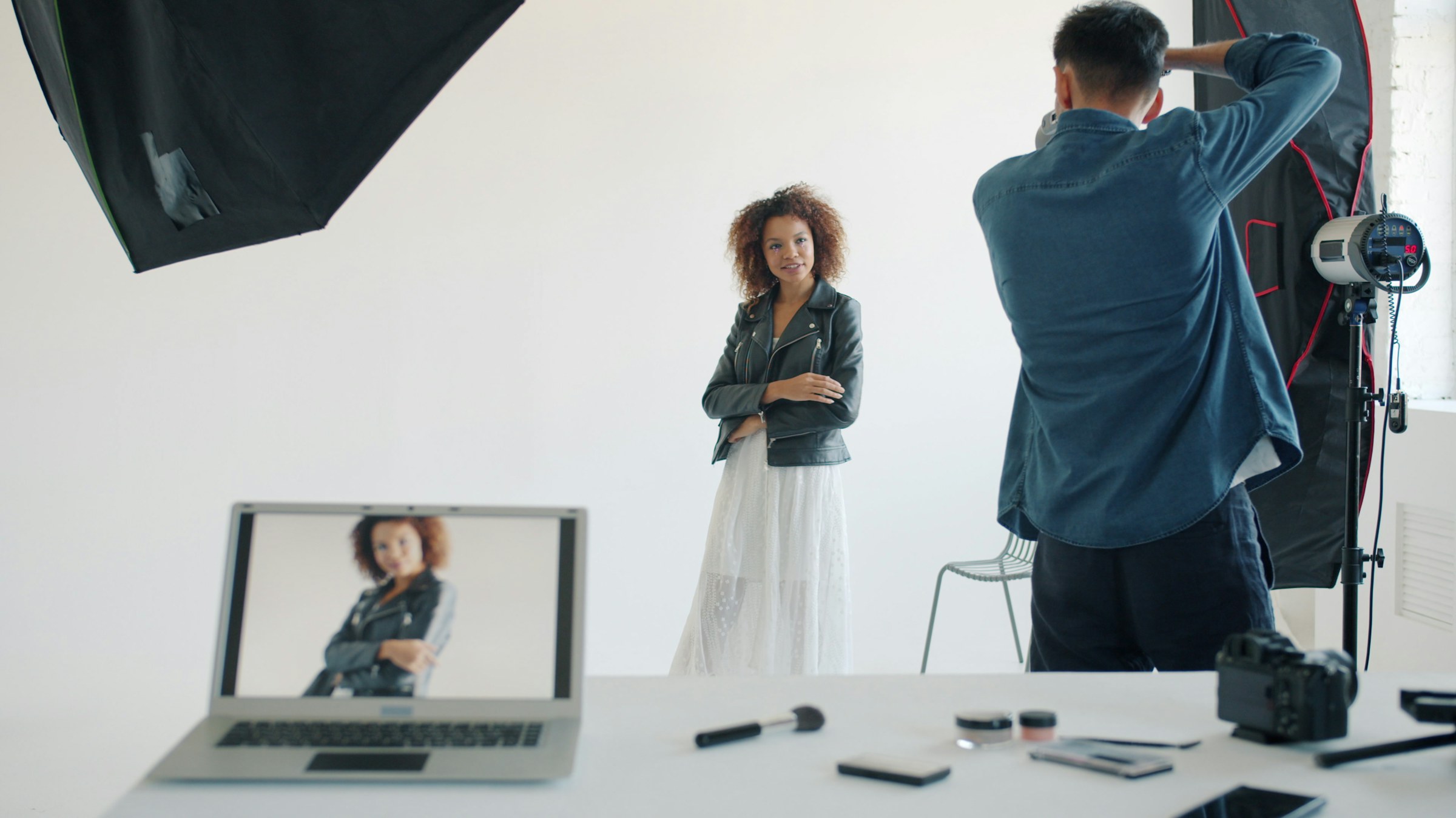 Fotograf fotografiert ein Model im Studio, während die Aufnahme auf einem Laptop sichtbar ist. Foto: Vitaly Gariev, Unsplash.