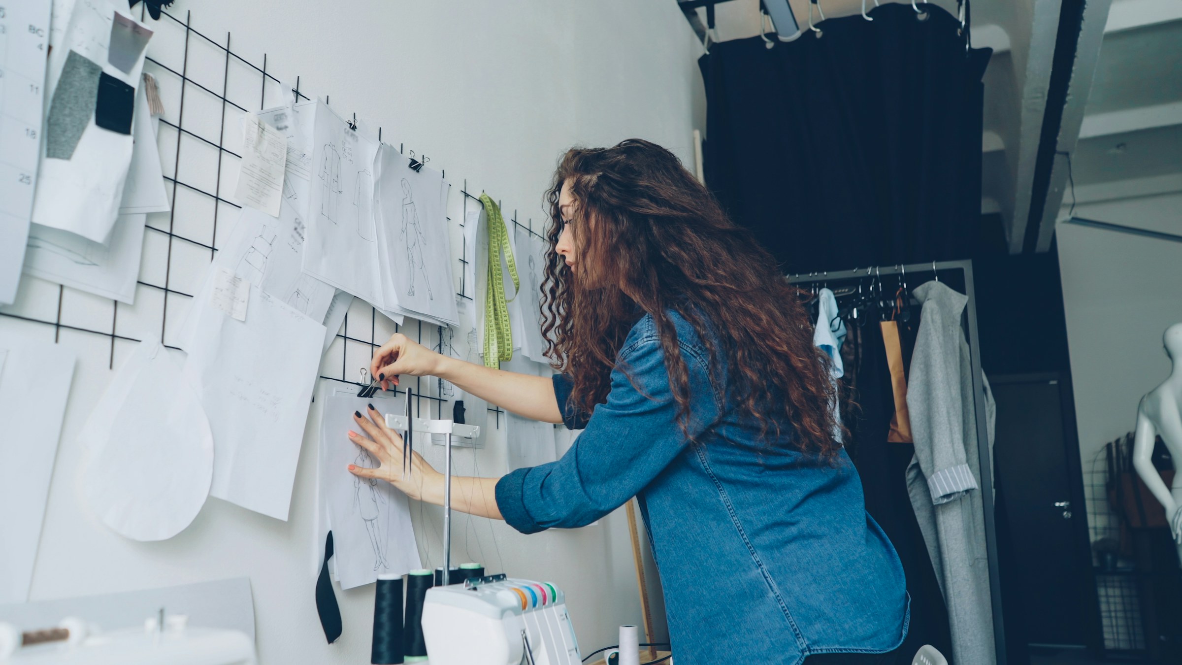 Designerin entwickelt eine visuelle Richtung an einer Wand mit Skizzen und Entwürfen. Foto: Vitaly Gariev, Unsplash.