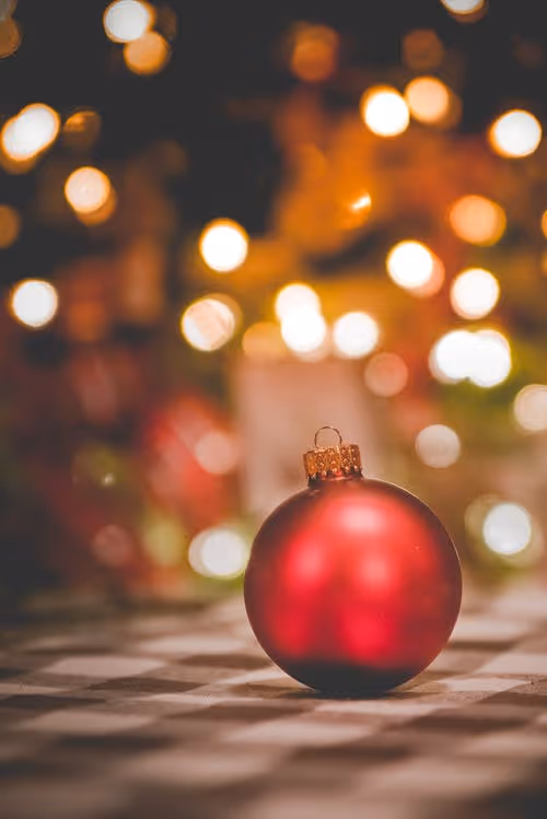 Red ornament with Christmas lights in the background
