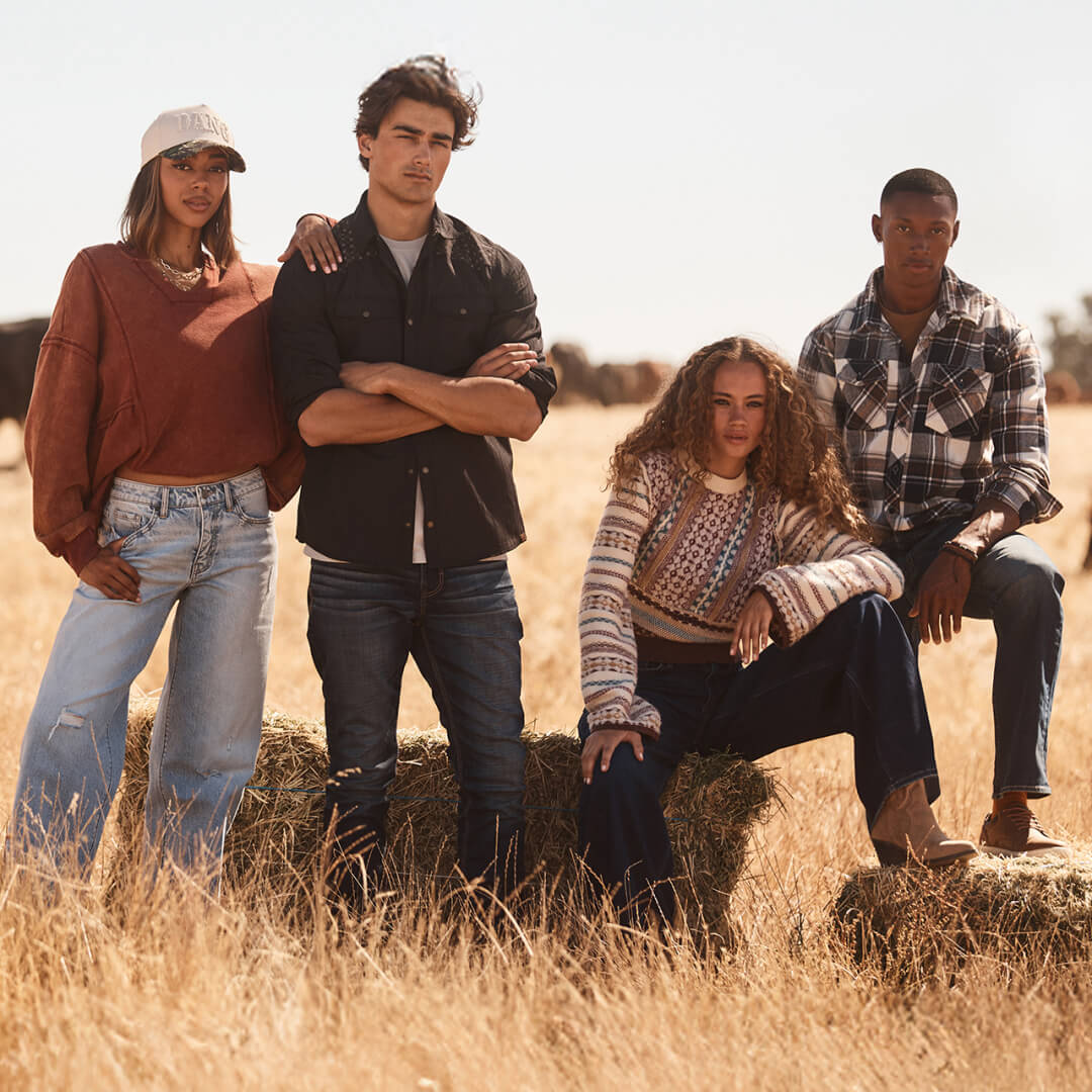 Four models in a hay field wearing Buckle denim jeans