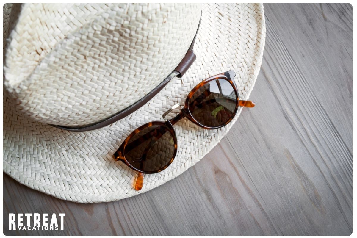 Stylish hat and sunglasses resting on a rustic wooden surface, evoking a relaxed vibe for summer and spring adventures.