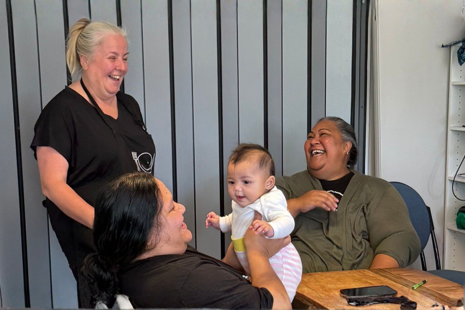 A māmā, pēpi, and WELLfed staff share a moment of joy.