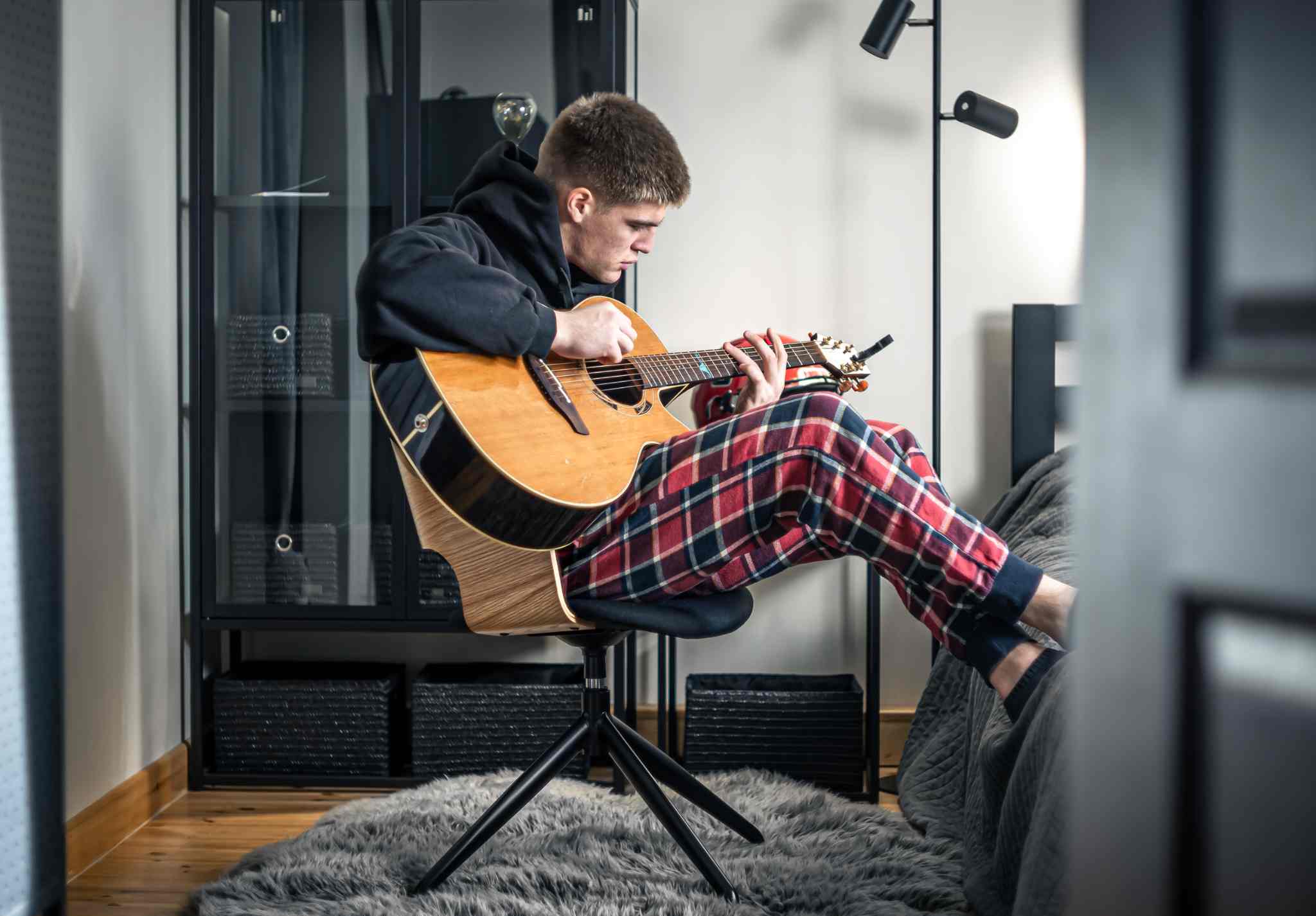 Mladý muž hraje na akustickou kytaru v bytě, hudba jako jeden z častých důvodů stížností sousedů na hluk.
