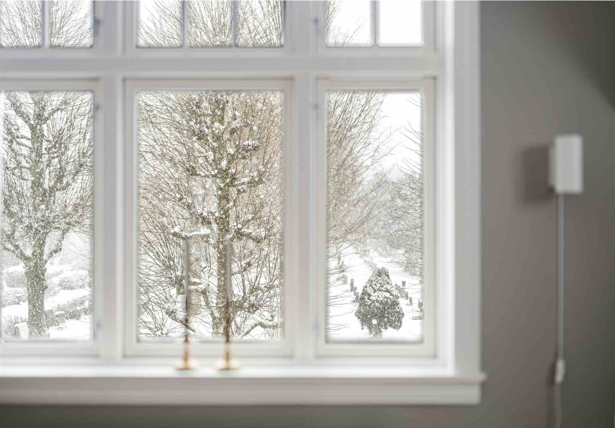 Pohled z plastového okna v zimním režimu do zasněžené krajiny – zimní nastavení oken pro lepší těsnění a úsporu tepla.